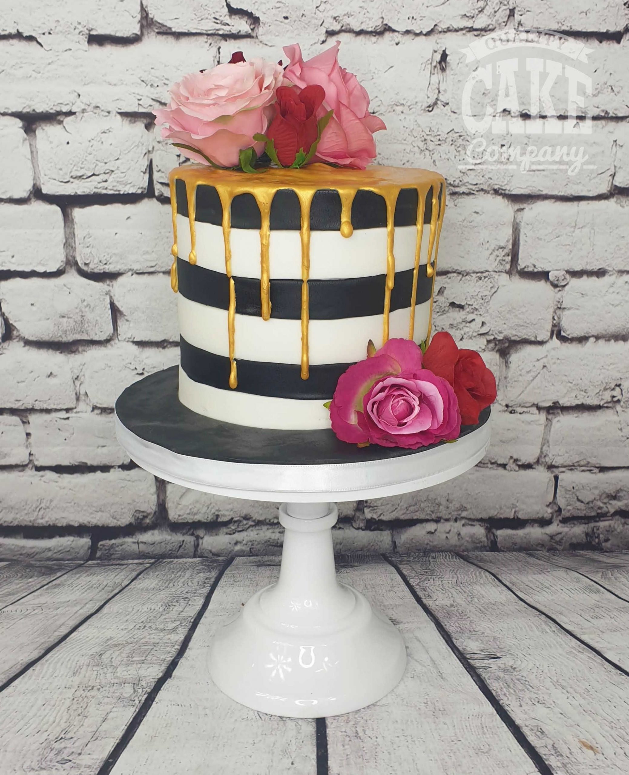 Black and purple theme cake with fondant flowers and gold drip .