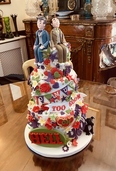 Two groom figures sat on top of decorated multi tier cake