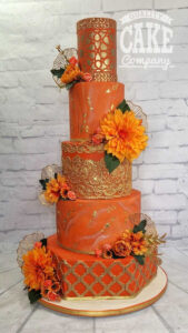 five tier burnt orange wedding cake with gold lace details and large flowers